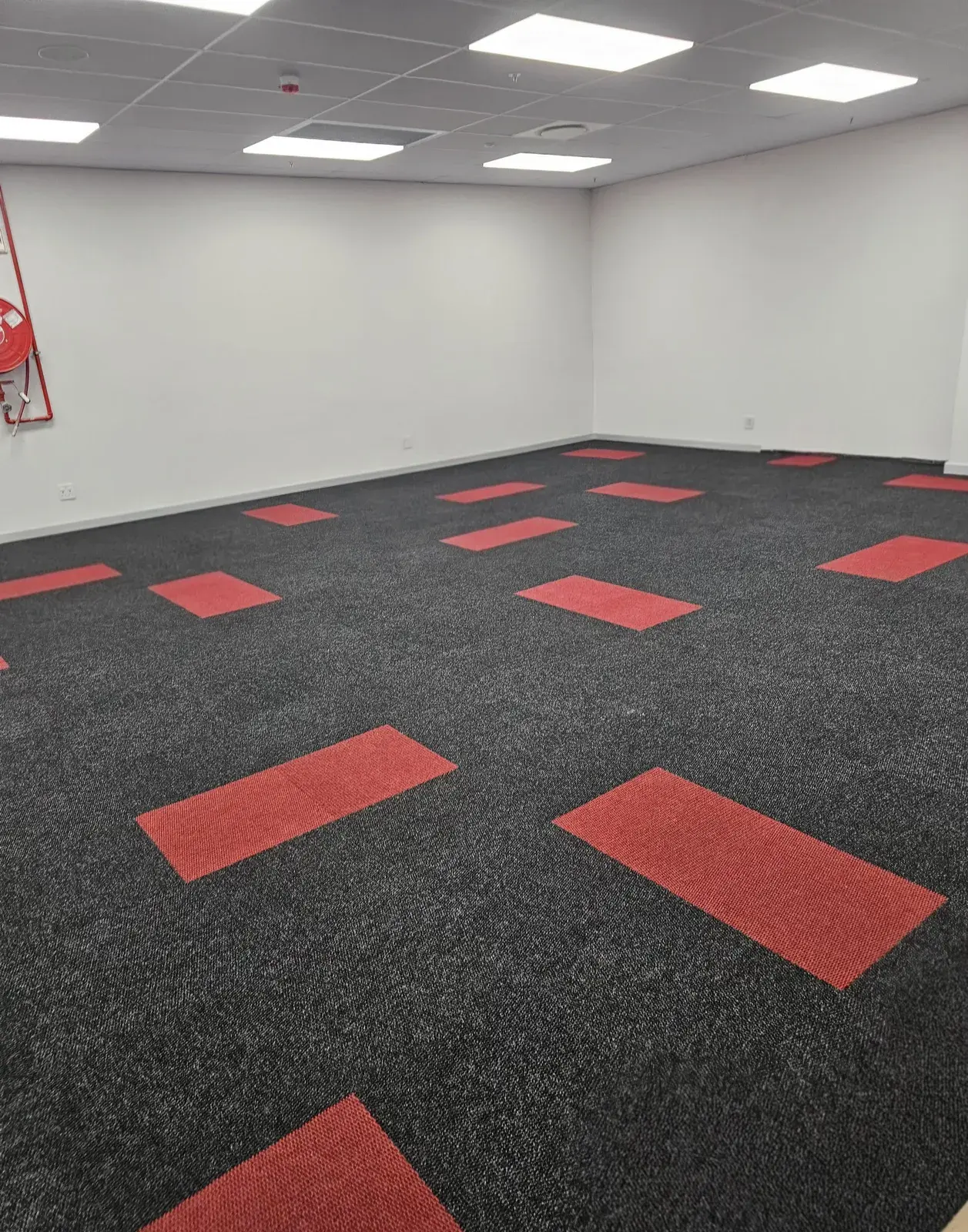 An empty office floored in charcoal carpet tiles with red accent tiles set through it.