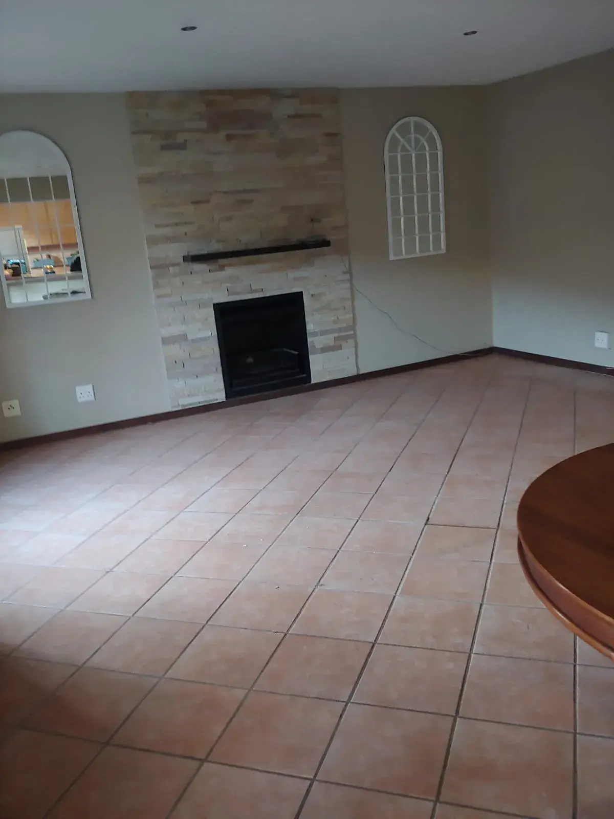 A living room with a stone-clad fireplace, floored in terracotta ceramic tiles.