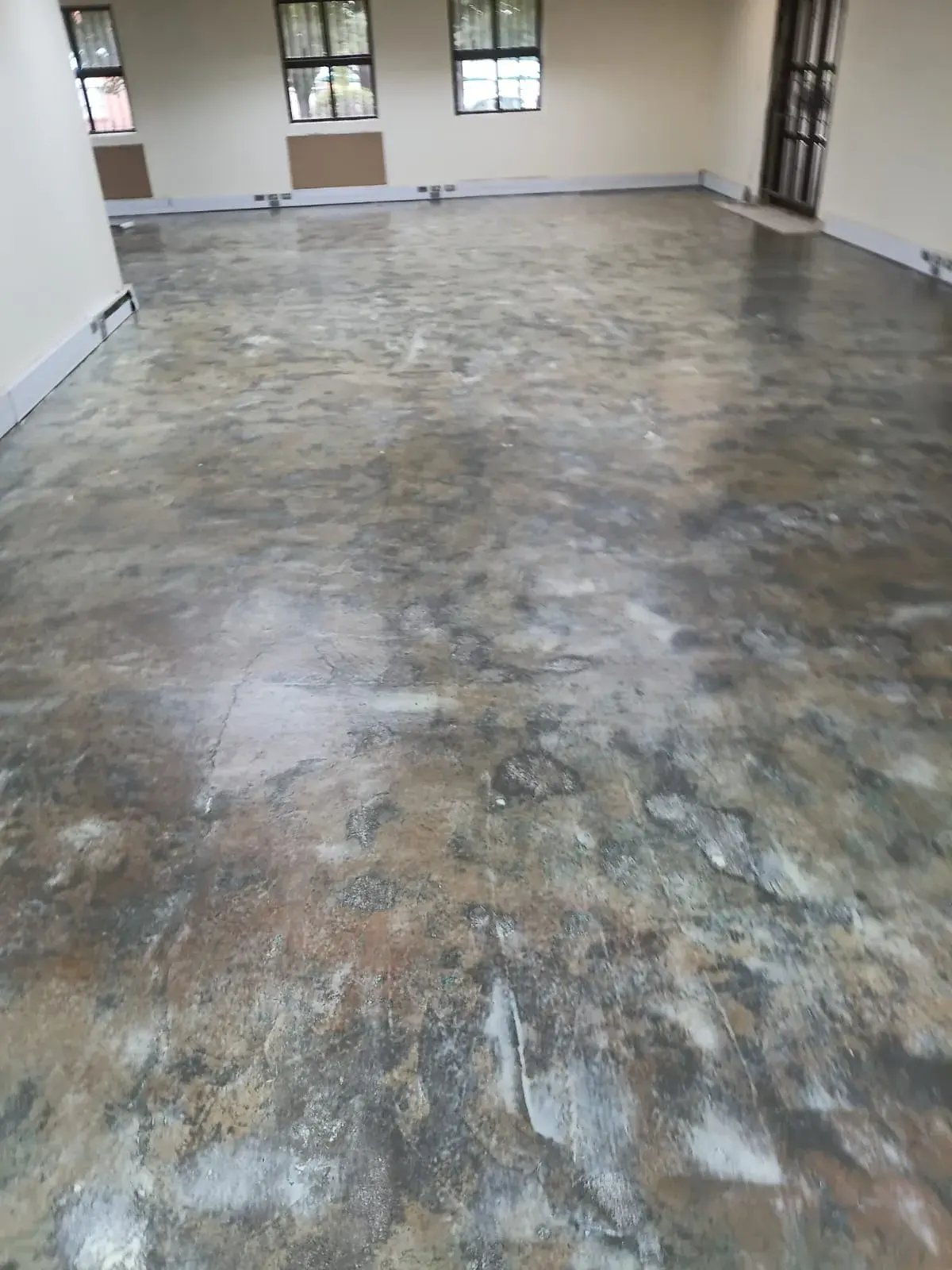 An empty office with the old floor lifted: a bare, patchy concrete slab with adhesive marks.